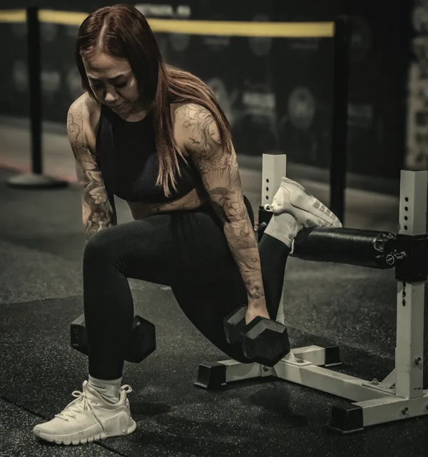 An adult HAUS member holding dumbbells in a rear-foot-elevated split squat